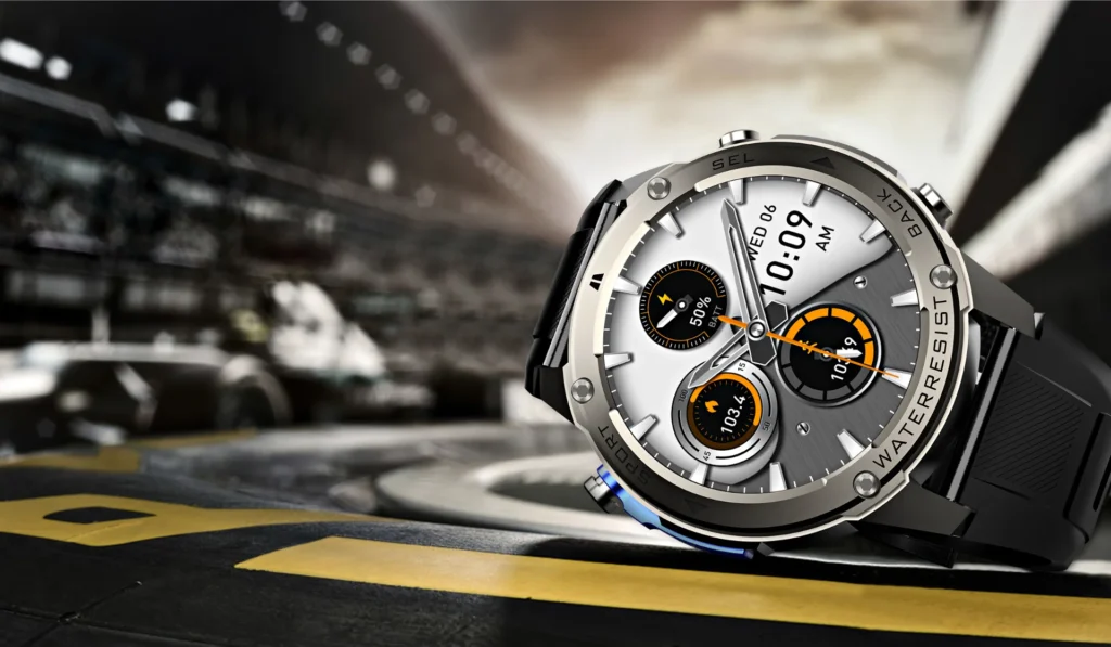 Silver and black smartwatch with digital display, showing time and date, placed on a race track with blurred racing cars in the background.