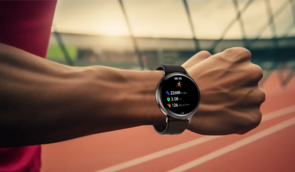 A person's wrist wearing a smartwatch showing fitness metrics like steps, distance, and heart rate while standing on a running track.